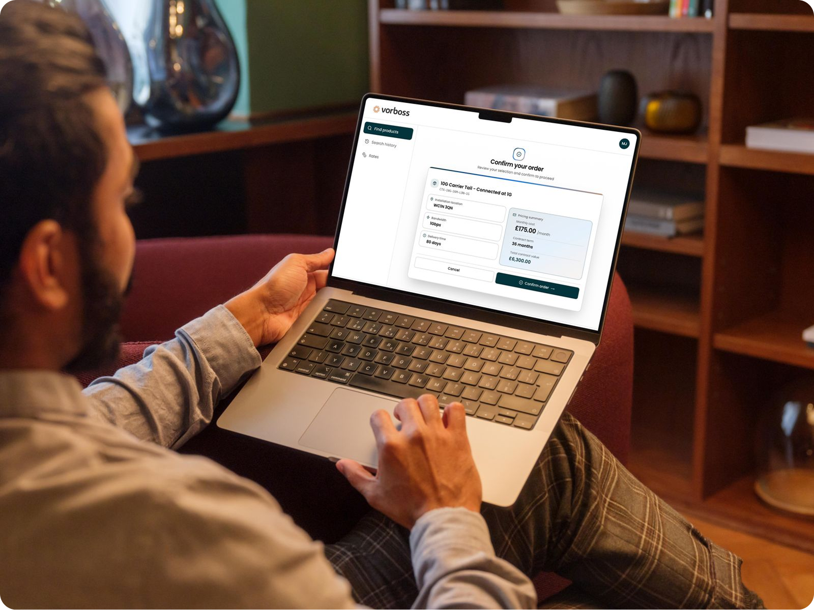 Two people reviewing technical drawings and a laptop screen showing a carrier confirmation order summary.
