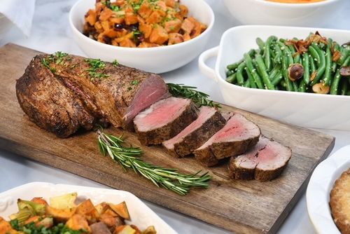 Sliced filet on a cutting board surrounded by bowls of vegetable sides