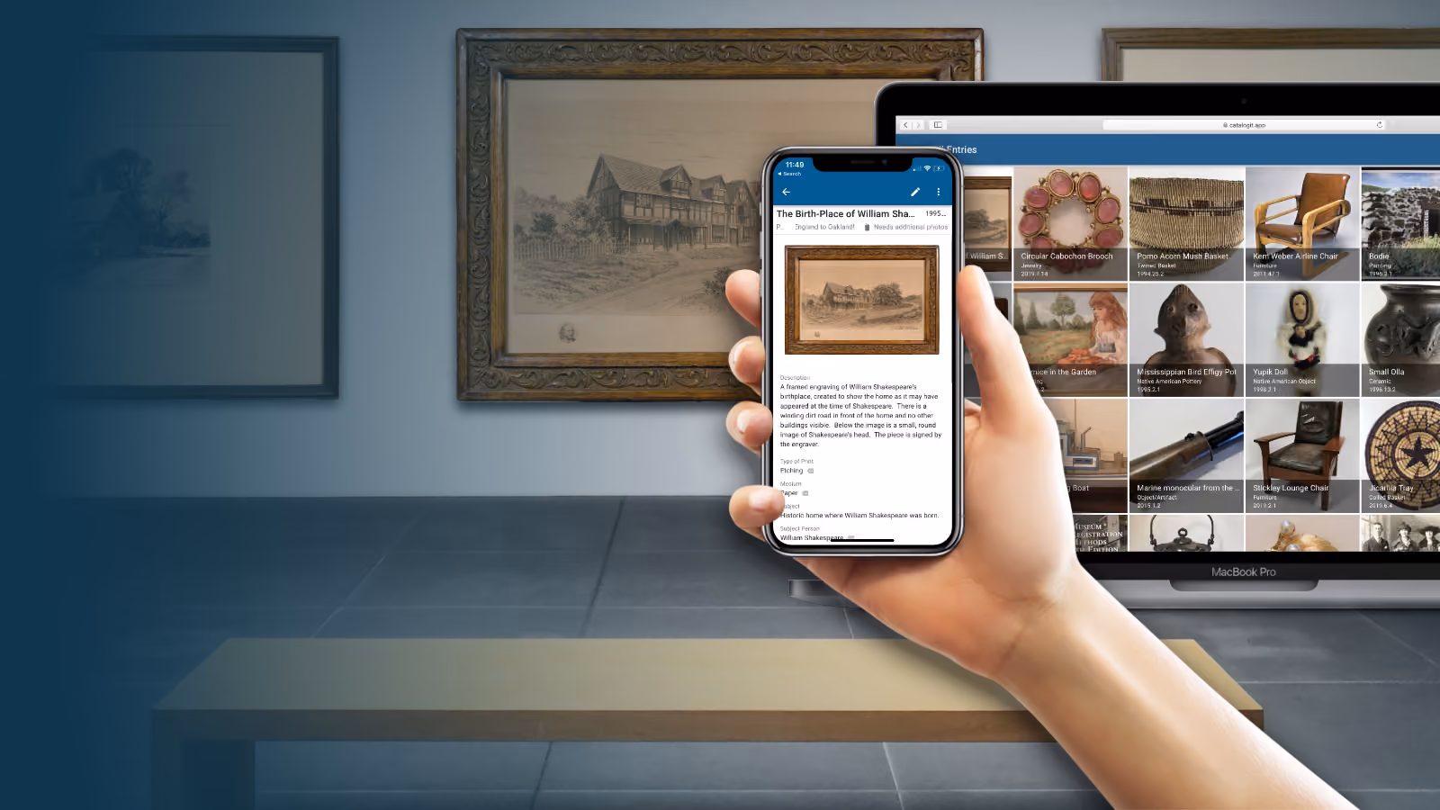 Hand holding a mobile phone displaying a CatalogIt entry of an artwork with the framed engraving in the background and a laptop screen showcasing a digital collection.