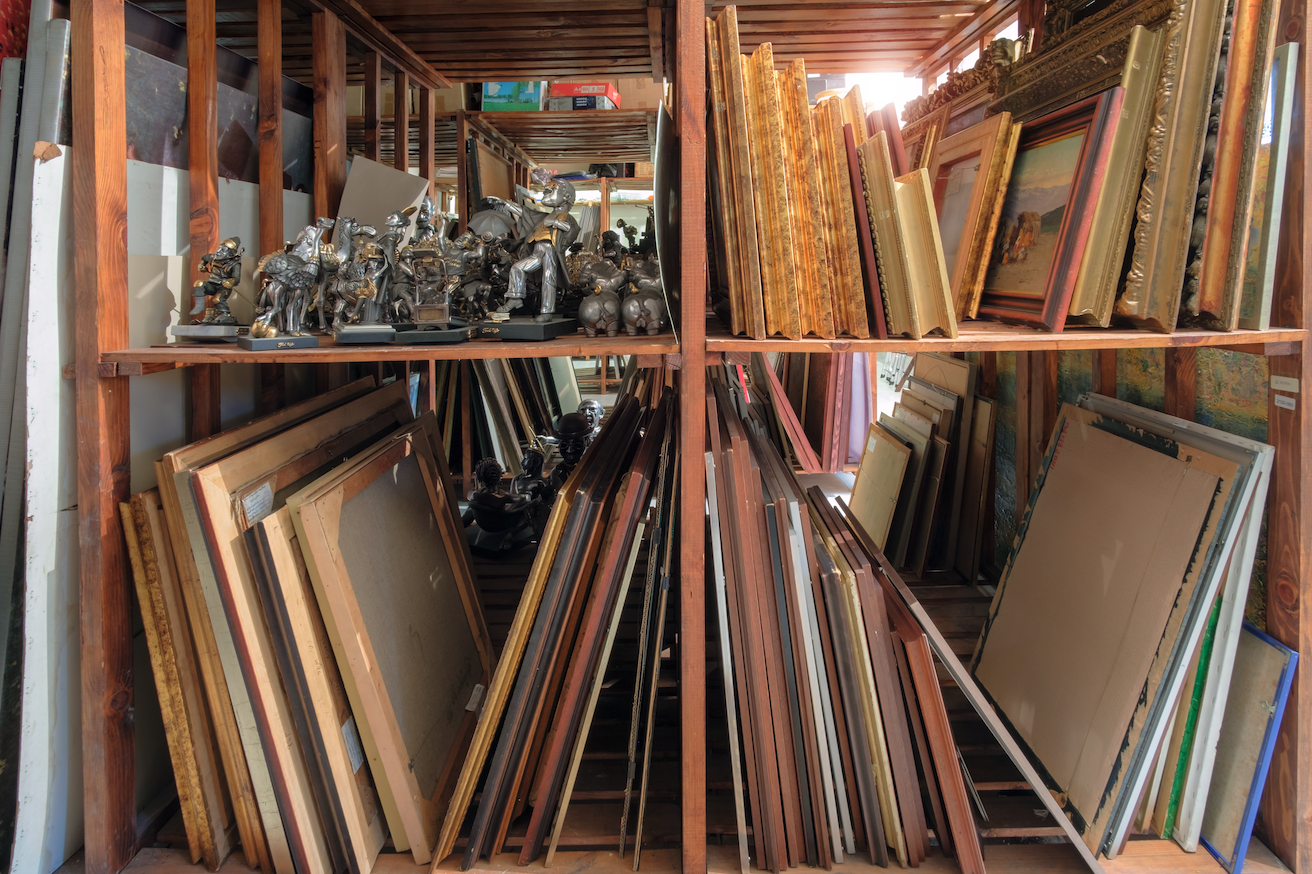 Storage area filled with various framed artworks organized on wooden shelves. Image courtesy of Shutterstock.