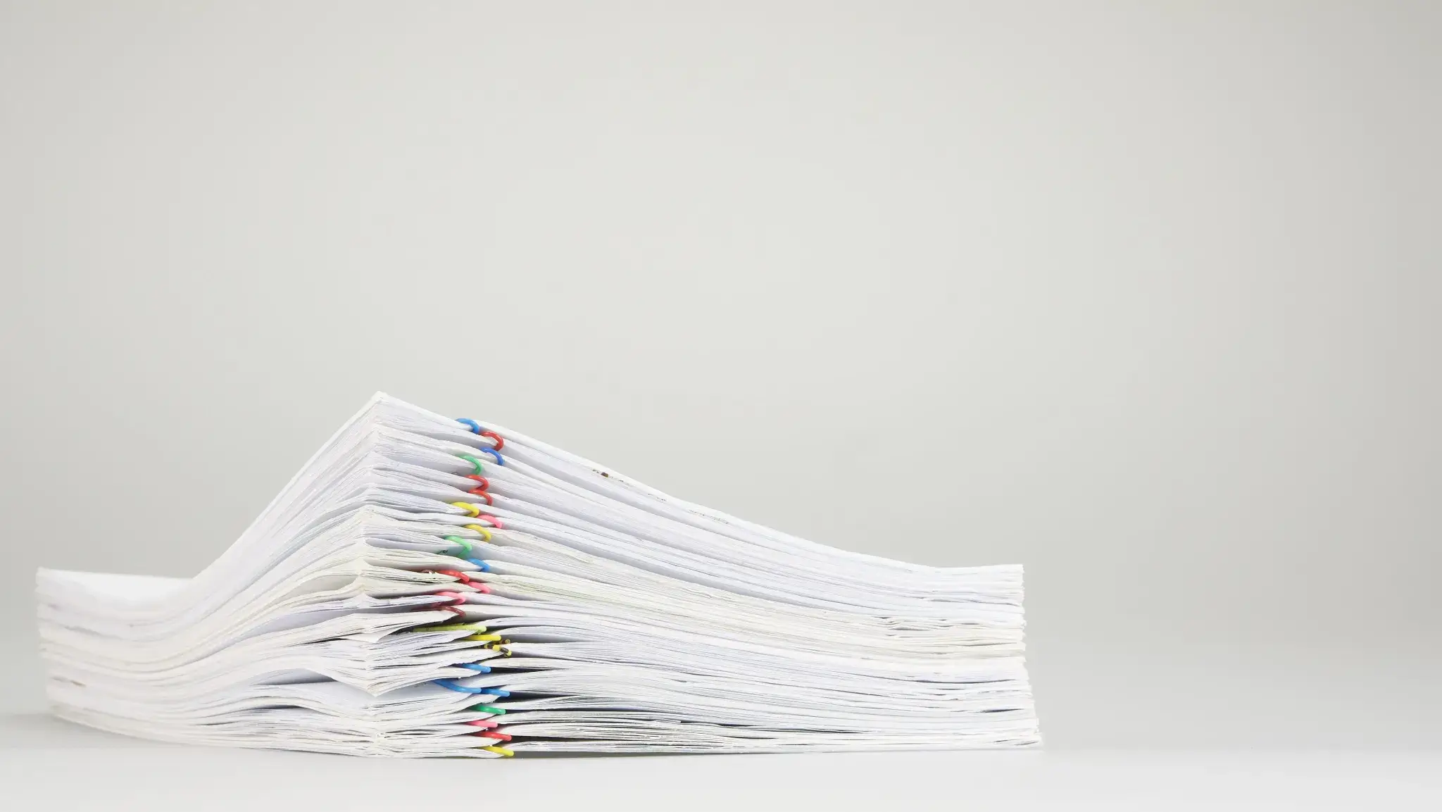 Stack of paper documents held together with colorful paper clips on a white background. Image courtesy of Adobe.