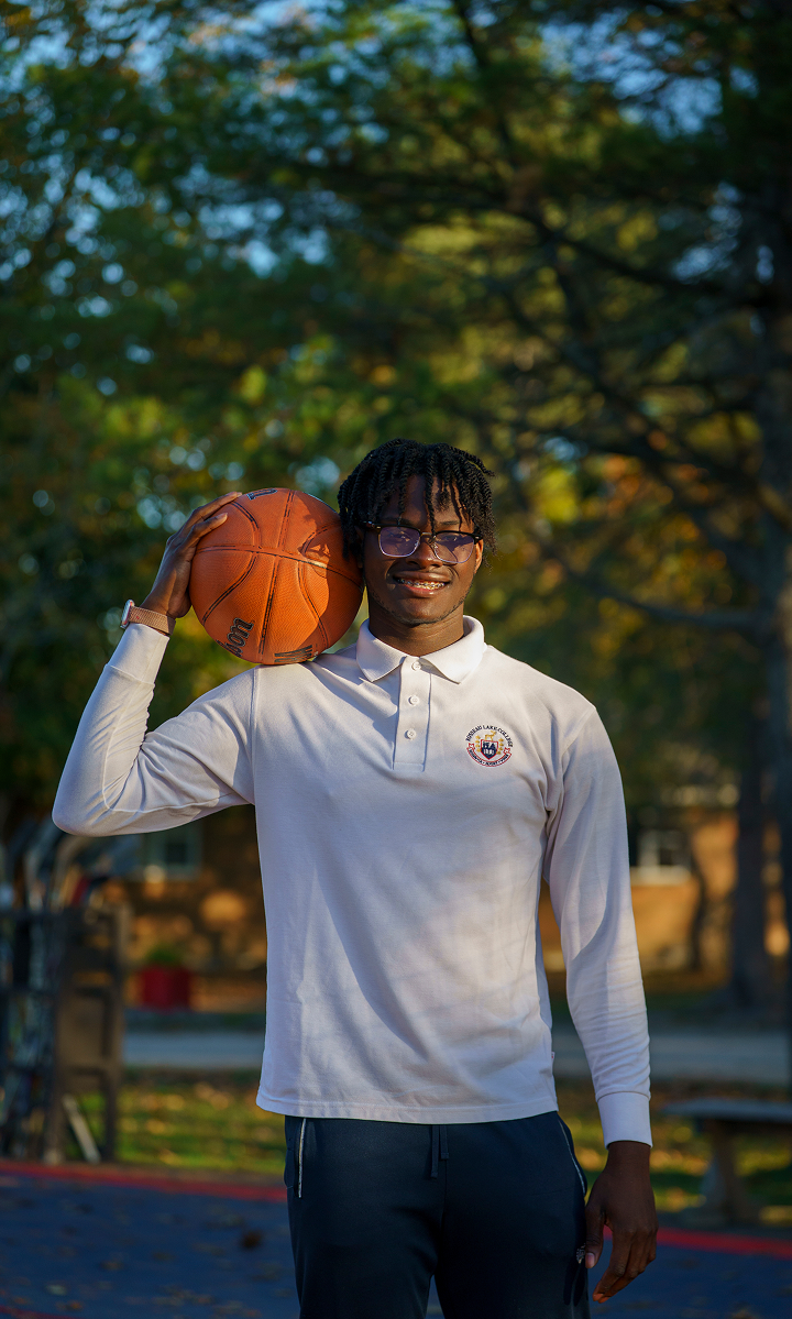 A teenage boy in Rosseau Lake College uniform is holding a basketball