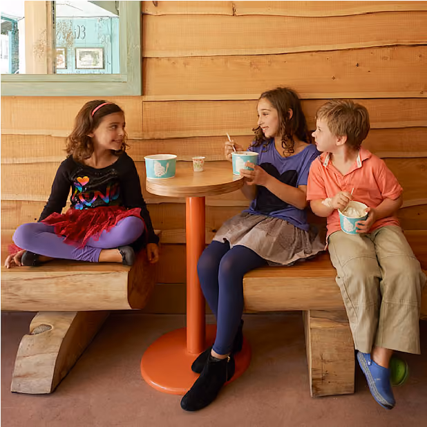 Photo of three young children sitting at a table eating frozen yogurt.