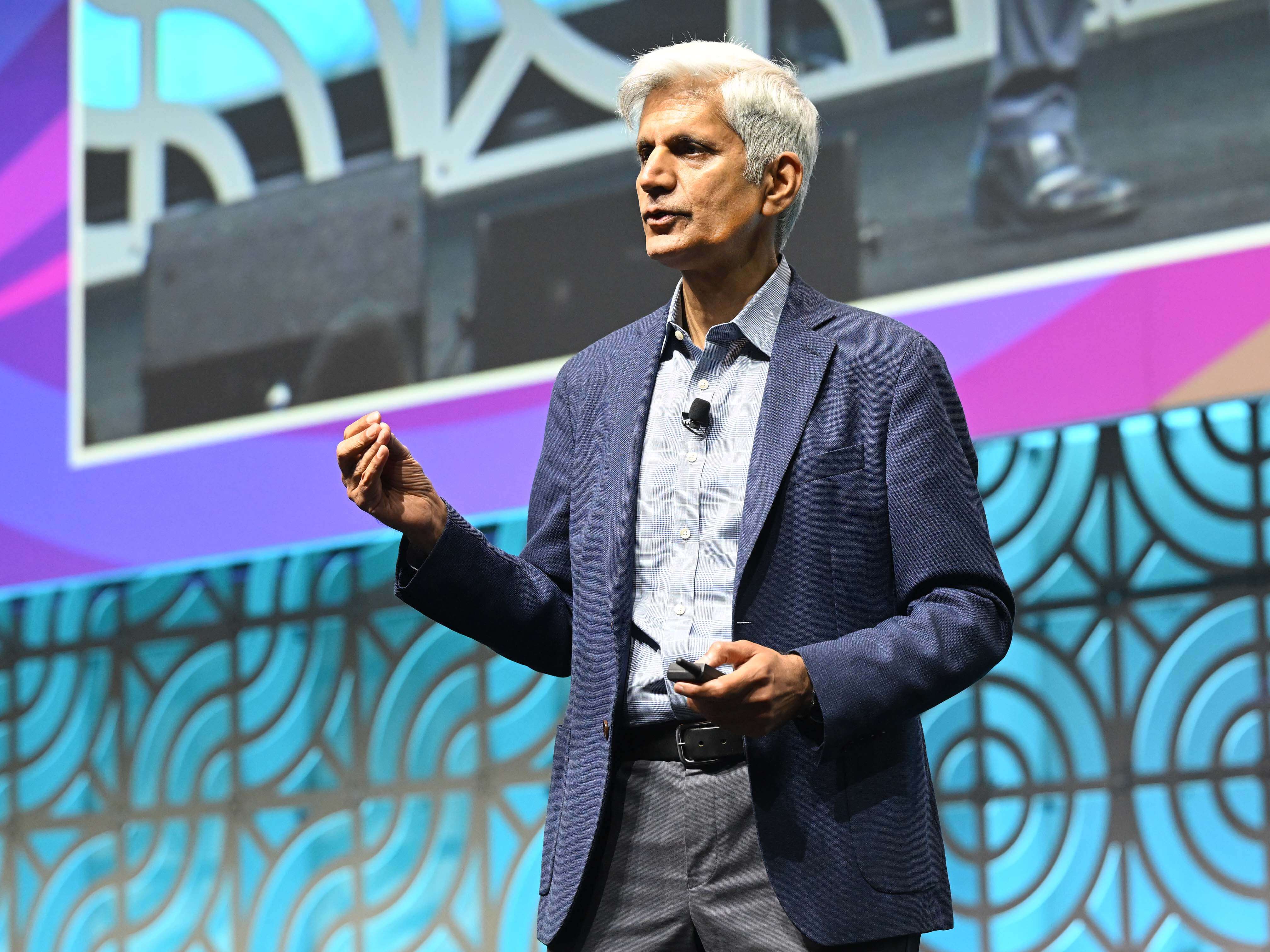 Dr. Hitendra Wadhwa in a navy blazer presenting on stage at ATD Conference, gesturing with one hand against a patterned blue background.