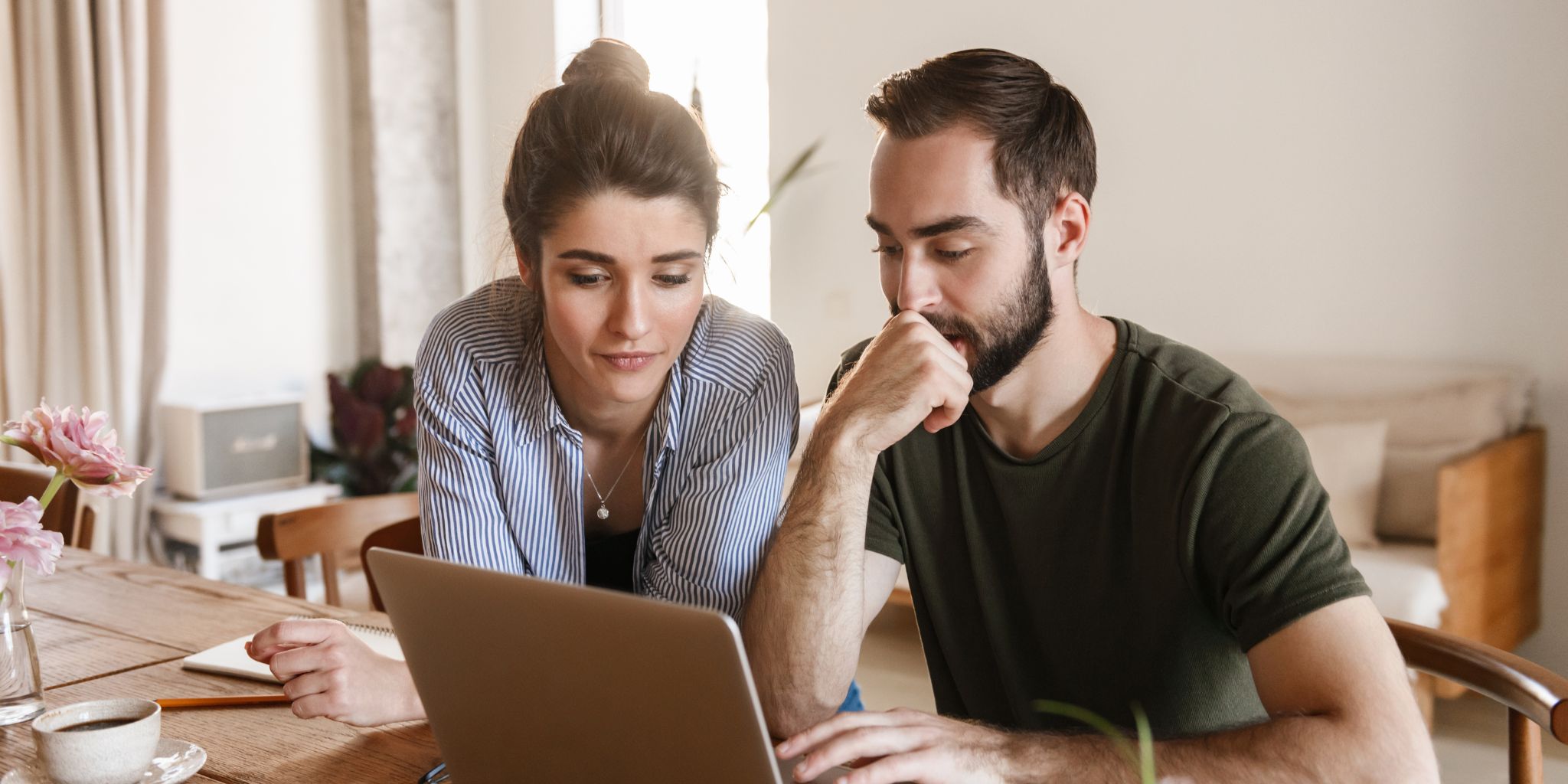  A tradie couple sitting together at a kitchen table, focused on a laptop screen, reviewing their business finances and planning their next steps.