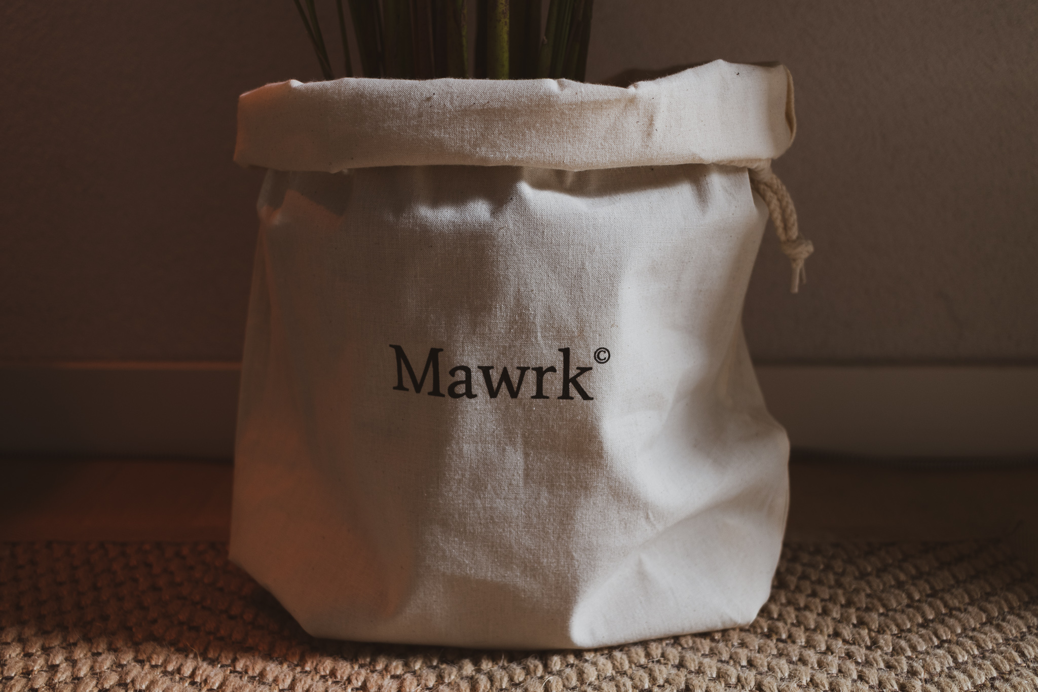 A cotton pouch with Mawrk logo fitted around the foot of a plant.