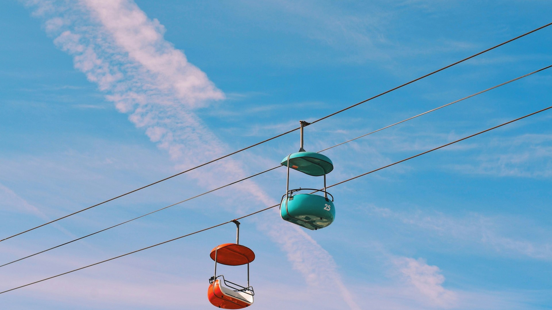 Zwei Seilbahn-Gondeln an gespannten Drahtseilen vor blauem Himmel, Sinnbild für Kommunikation als Brücke zwischen Strategie und Teams