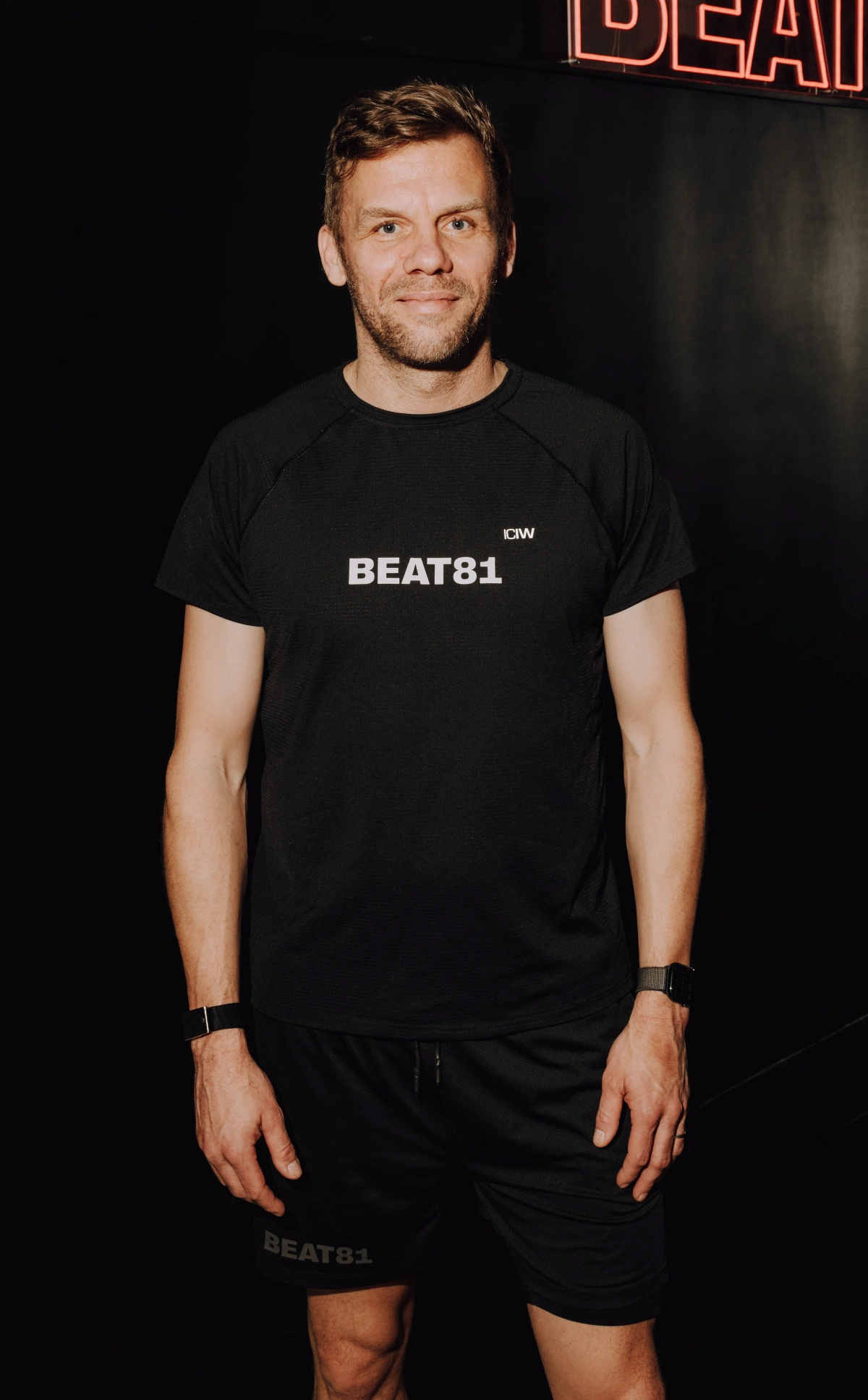 Der CEO steht in einem schwarzen BEAT81-T-Shirt und Shorts vor einem dunklen Hintergrund.