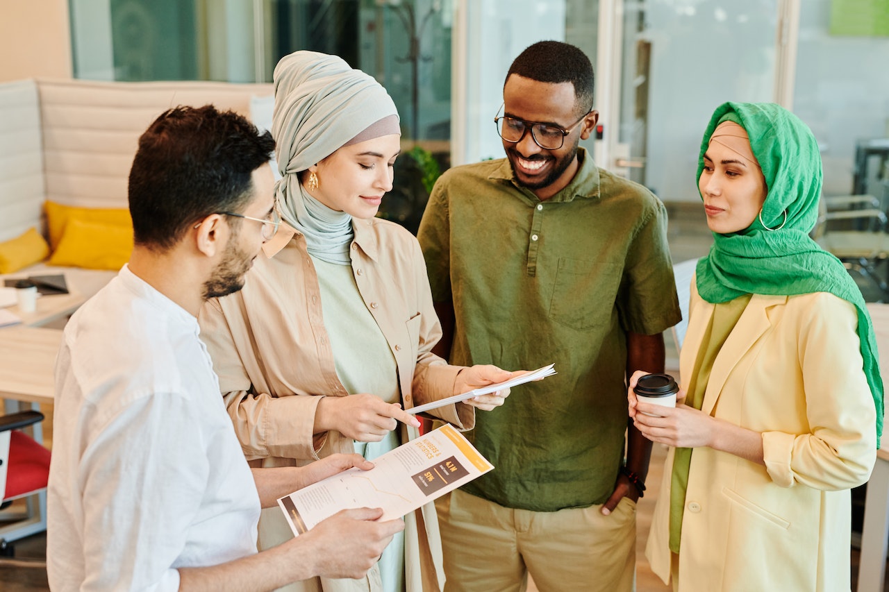 Photo of four people standing together, at work, having a conversation while looking at some papers
