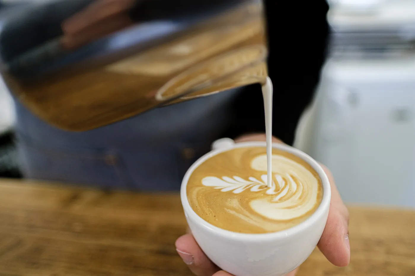 Een barista die latte art maakt met melk in een cappuccino.