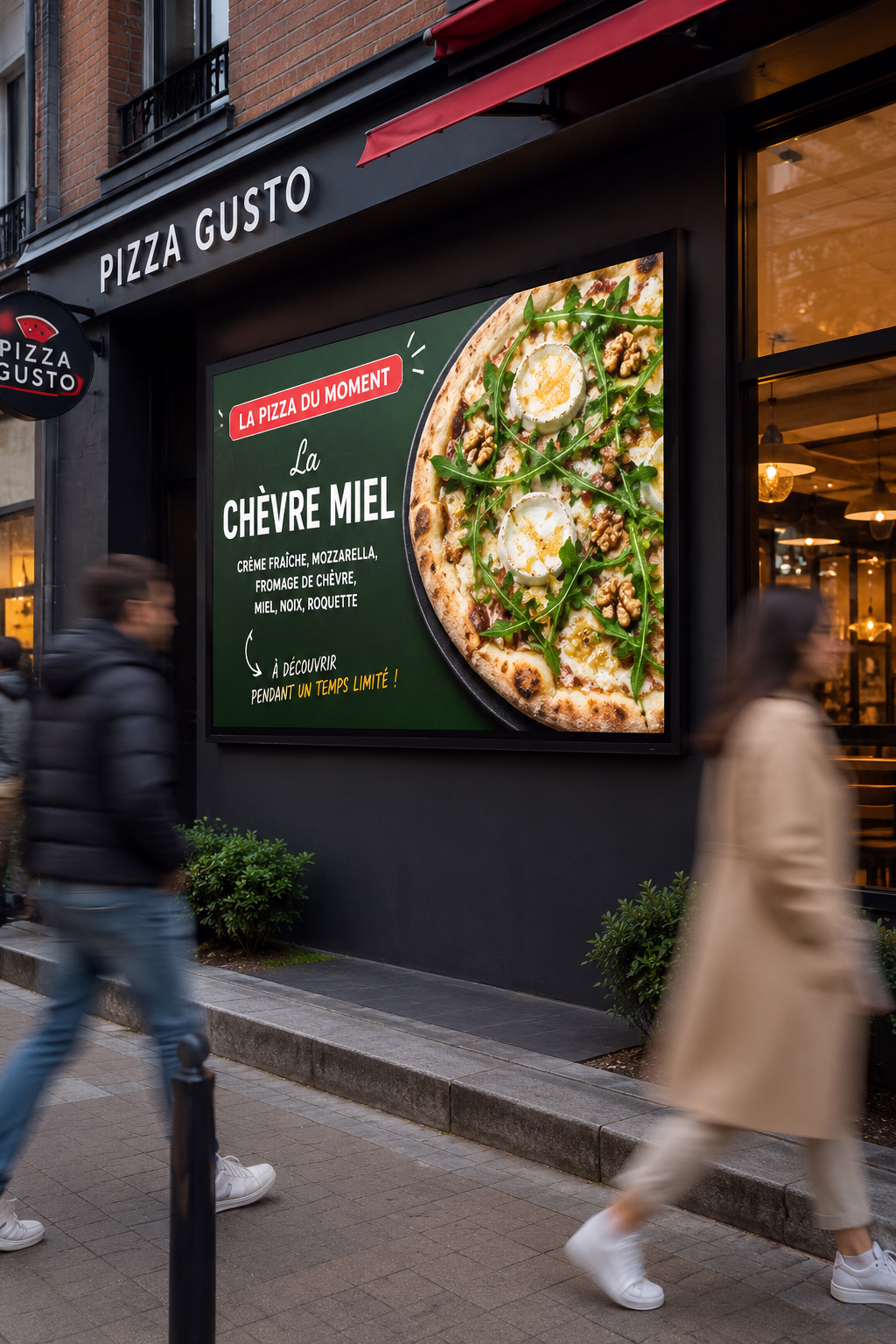 Écran d’affichage dynamique 16:9 installé à l’extérieur d’une pizzeria, présentant en français la pizza du moment « Chèvre Miel ». Des passants apparaissent en mouvement devant la façade, dans une ambiance urbaine éclairée par une lumière naturelle.
