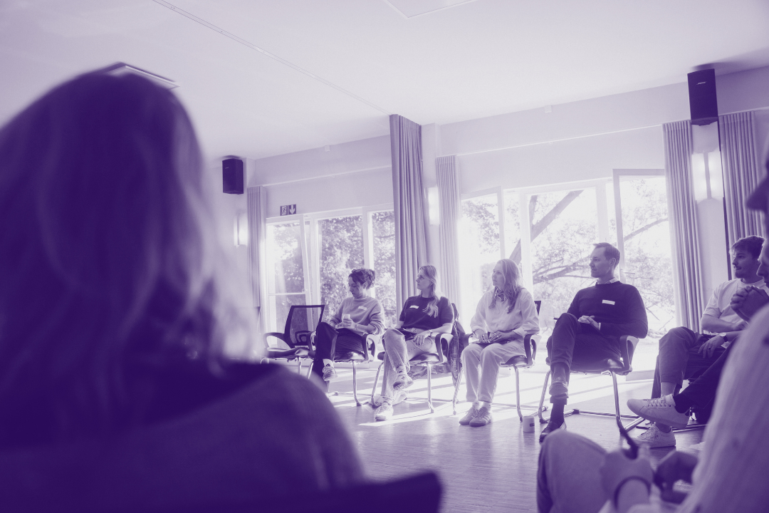 Eine Gruppe von Menschen sitzt im Stuhlkreis in einem hellen, sonnendurchfluteten Raum bei einem Workshop.