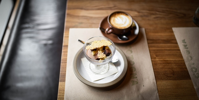 Bowl of dessert sitting next to a cup of cappuccino