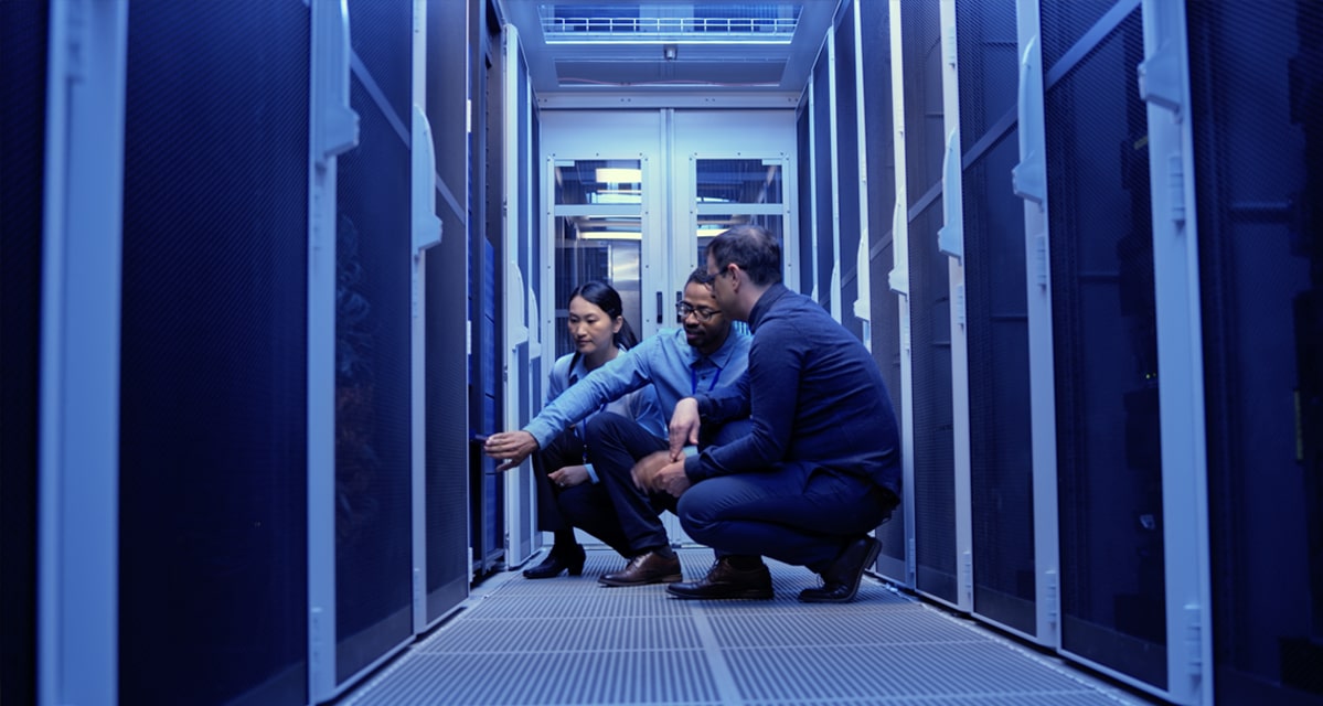 Two men and a woman in a server room inspecting the equipment