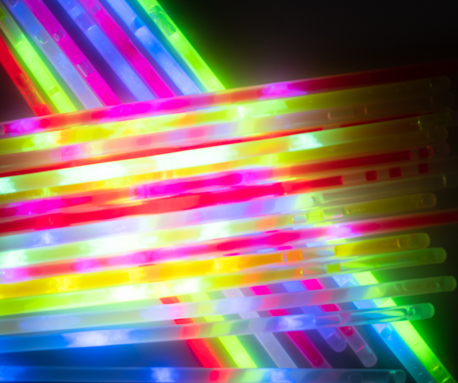 Close-up of overlapping fluorescent light sticks glowing in pink, green, blue and yellow.