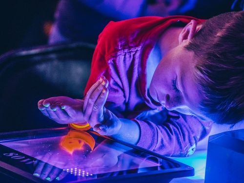 Child leaning over a black light, their nails painted and glowing, while bathed in blue and purple light