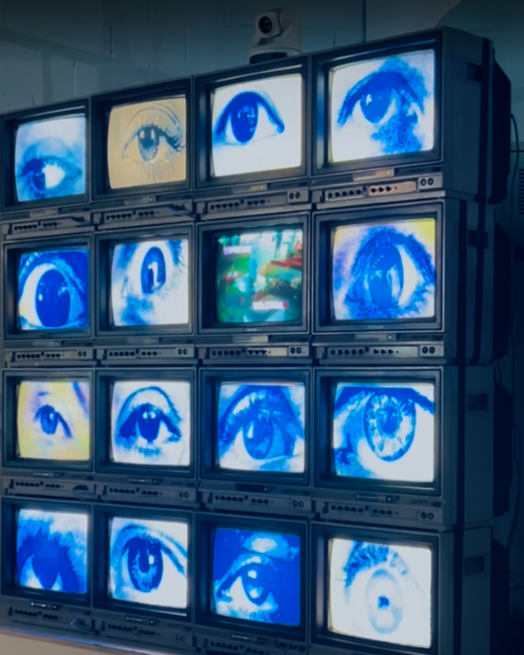 Wall of stacked vintage television screens displaying close-up images of human eyes in blue and white.