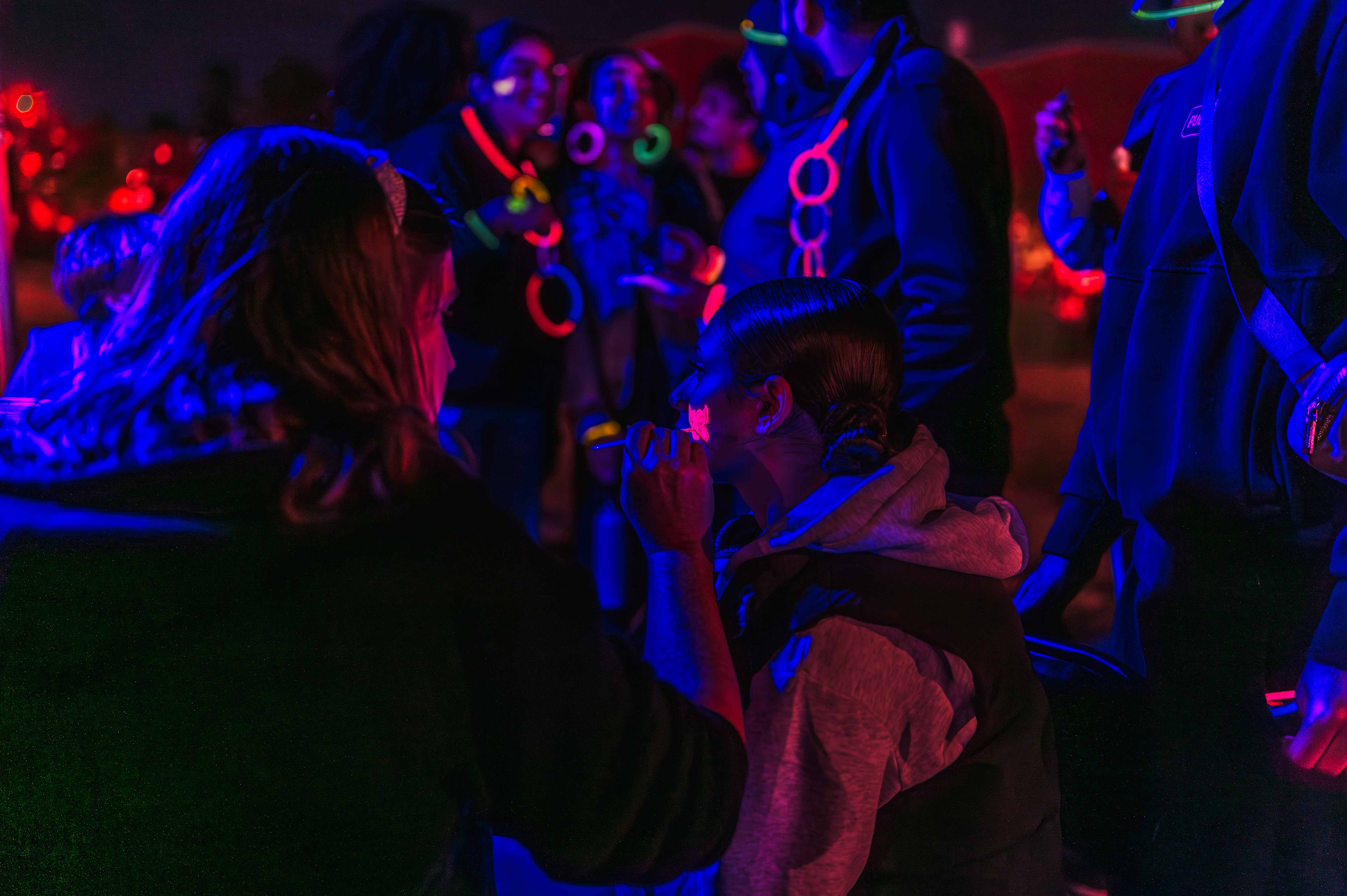 Festival attendees wearing and playing with colourful glowing accessories under blue and red light.