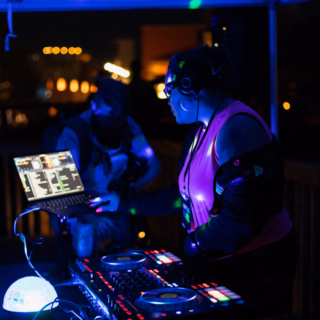 DJ performing at a night event, using a mixing console with vibrant blue and purple lighting.