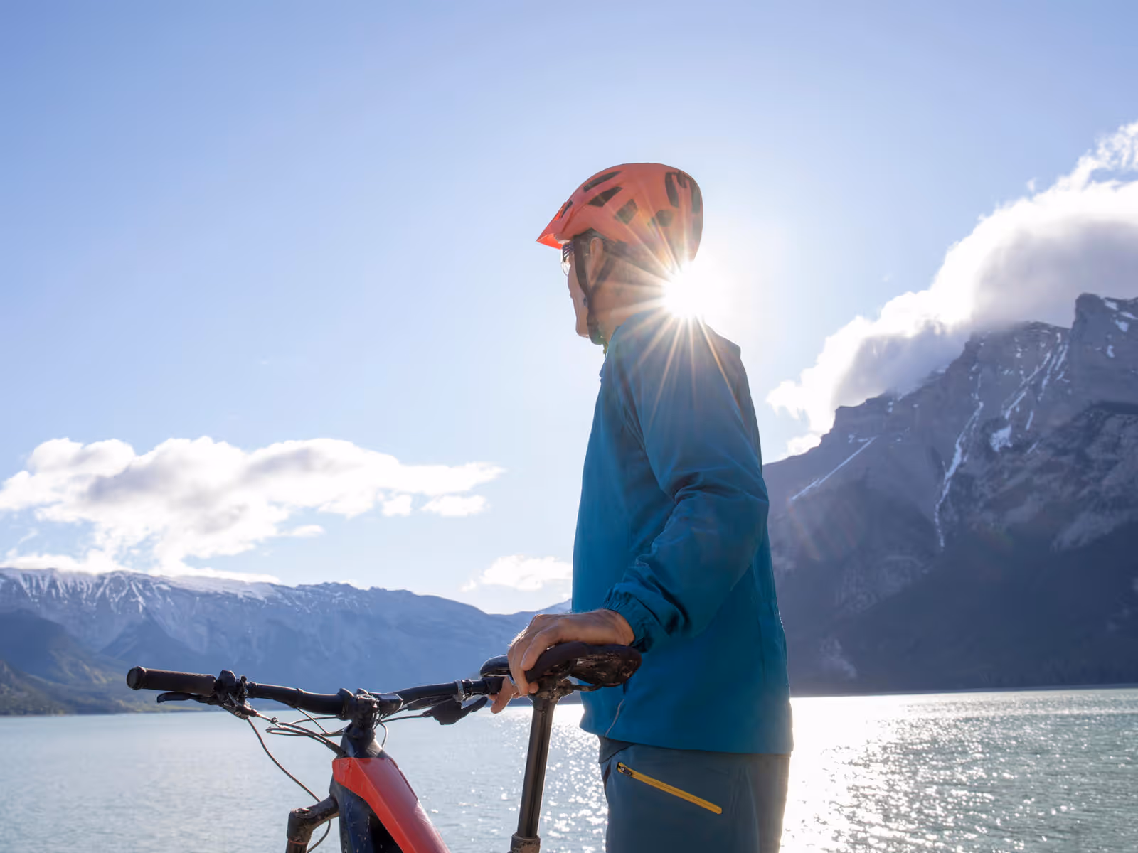 Man with bicycle in front of lake with mountains