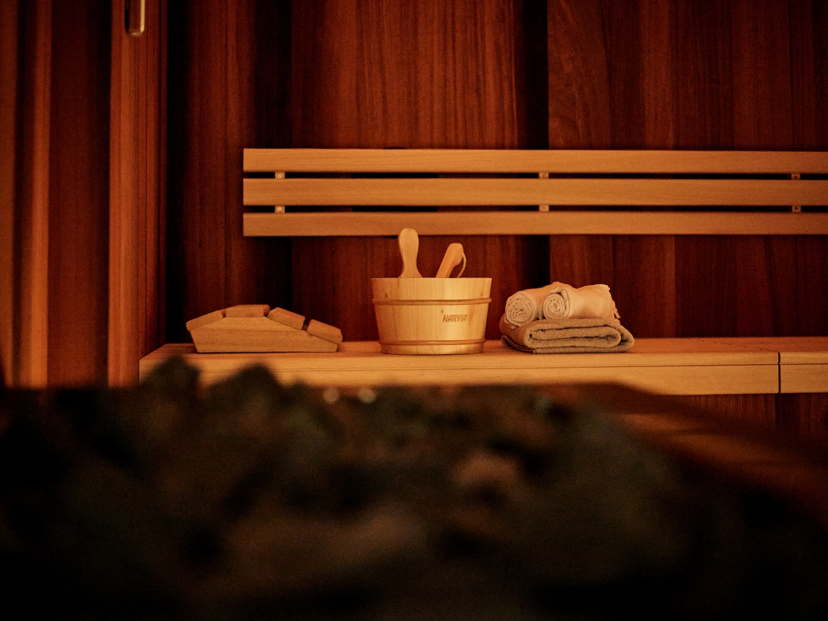 Un sauna en bois chaleureux, baigné d'une lumière tamisée, équipé d'accessoires traditionnels pour les projections d'eau et offrant une atmosphère de bien-être propice à la détente.