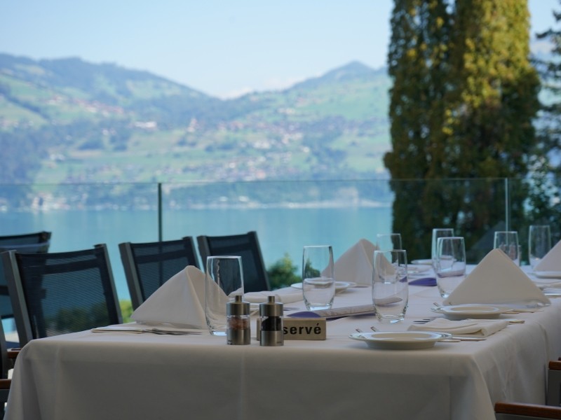 Vue sur la terrasse du restaurant, avec une table dressée de blanc et une vue sur le lac de Thoune
