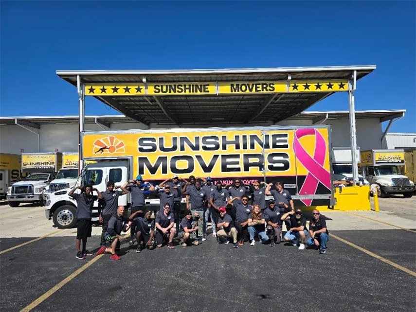 The Sunshine Movers crew in front of a pink breast-cancer-awareness moving truck