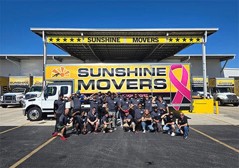 The full Sunshine Movers team in front of their headquarters and pink-ribbon truck