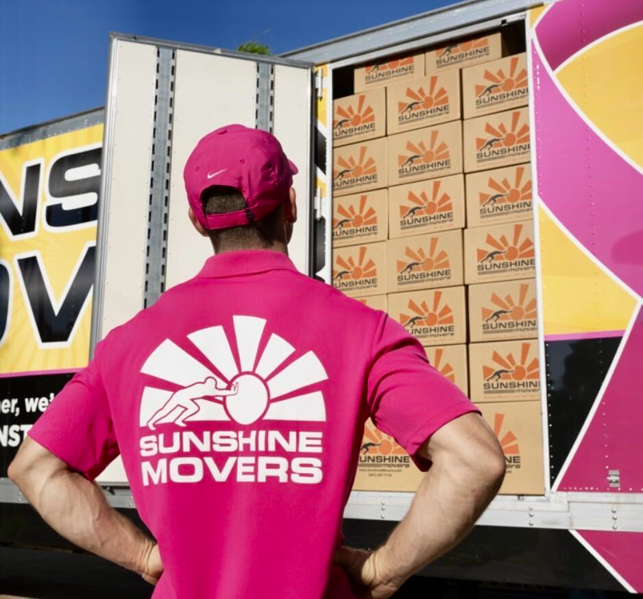 Sunshine Movers team member in a bright pink shirt beside a packed moving truck