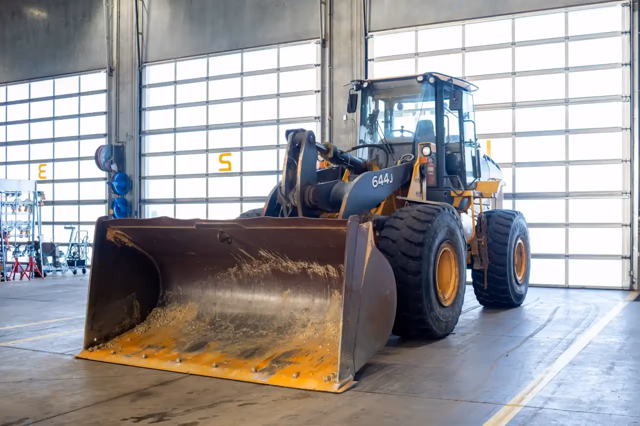 Wheel loader 644J inside service bay; scraped bucket and massive treaded tires ready for maintenance.