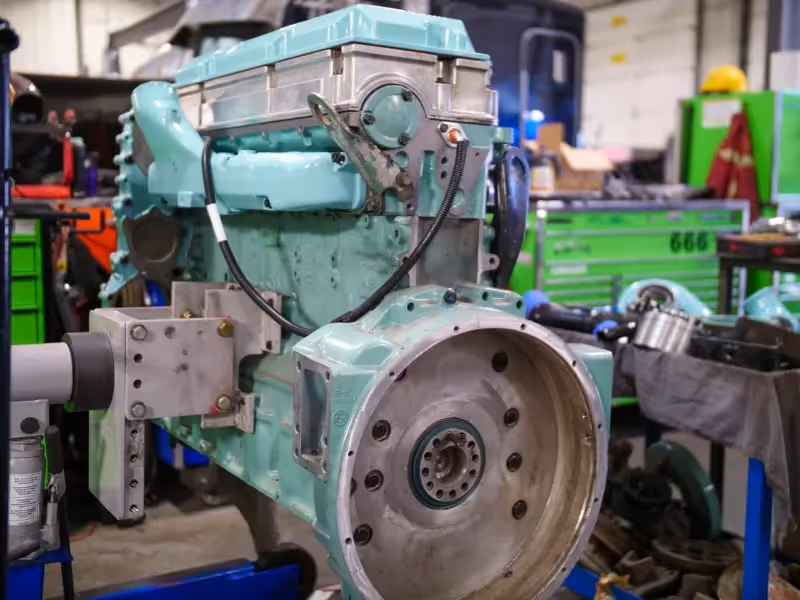 Diesel engine rebuild in progress with exposed flywheel housing inside a heavy-duty repair workshop.