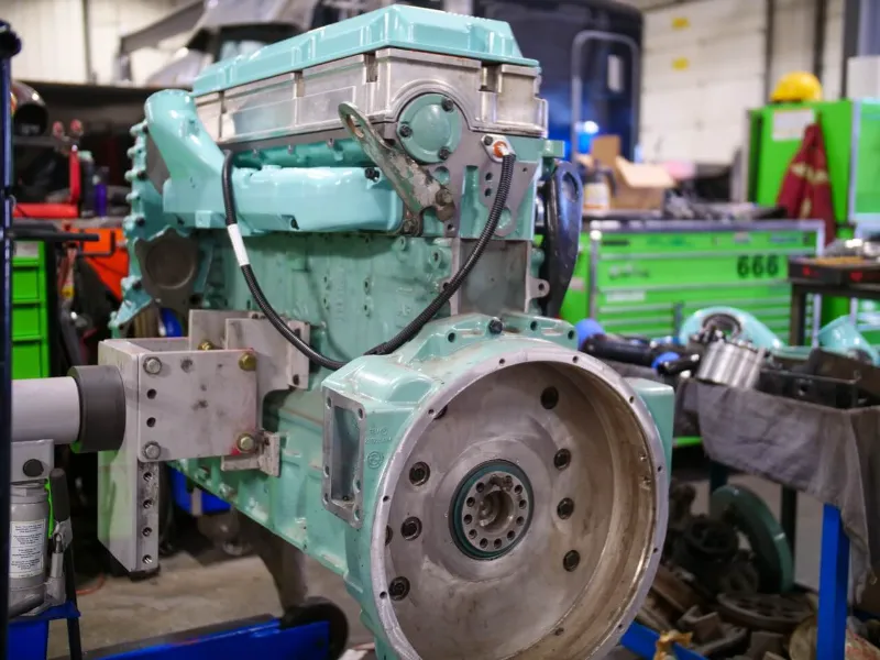 Diesel engine rebuild in progress with exposed flywheel housing inside a heavy-duty repair workshop.