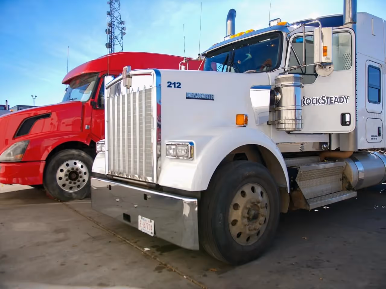 Heavy-duty truck repair: white Kenworth 212 with “ROCKSTEADY” beside red semi in lot.