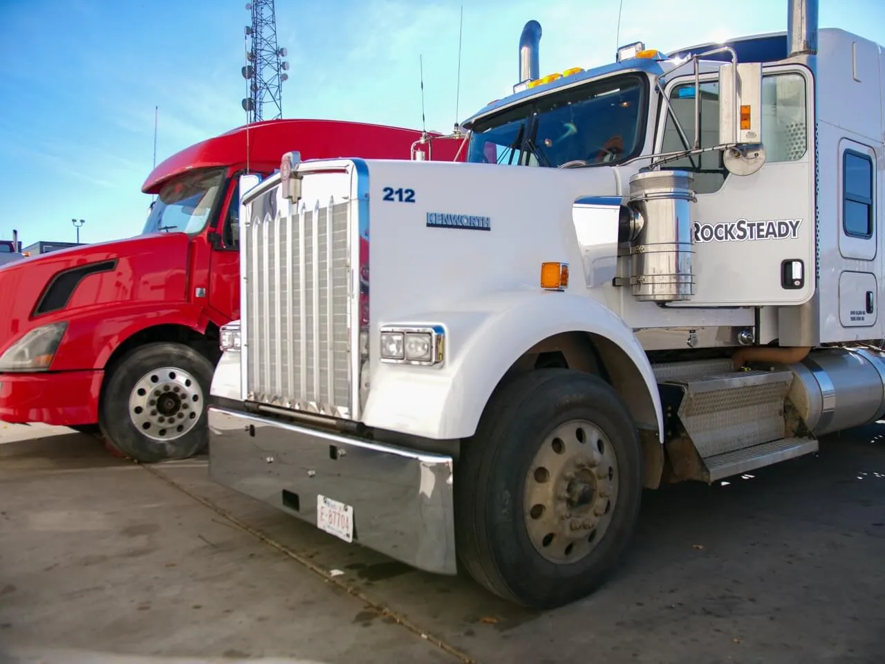 Heavy-duty truck repair: white Kenworth 212 with “ROCKSTEADY” beside red semi in lot.