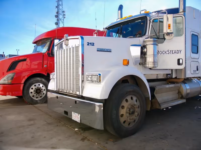 Heavy-duty truck repair: white Kenworth 212 with “ROCKSTEADY” beside red semi in lot.