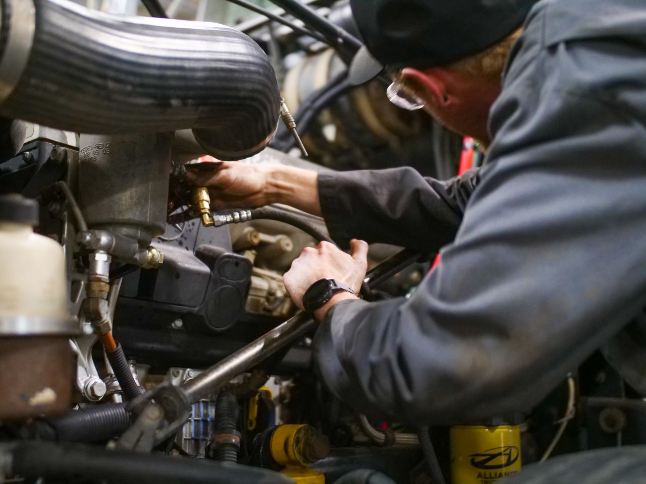 Diesel mechanic inspecting engine components and tightening fittings inside truck engine bay during repair service in workshop environment