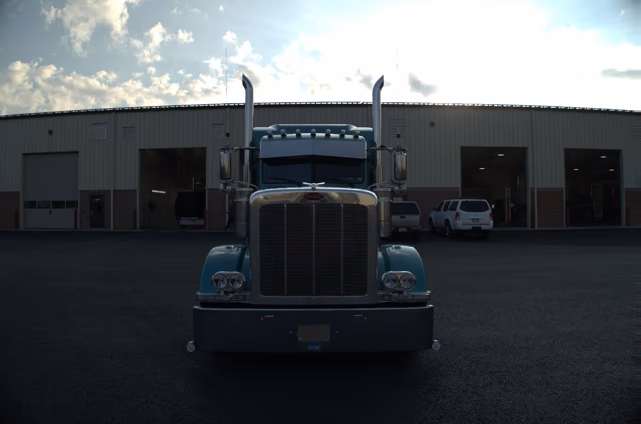 Front-facing semi truck parked outside a large diesel repair facility with open service bays under a cloudy evening sky.