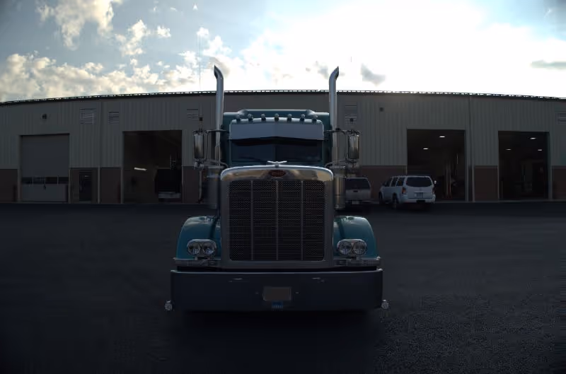 Front-facing semi truck parked outside a large diesel repair facility with open service bays under a cloudy evening sky.
