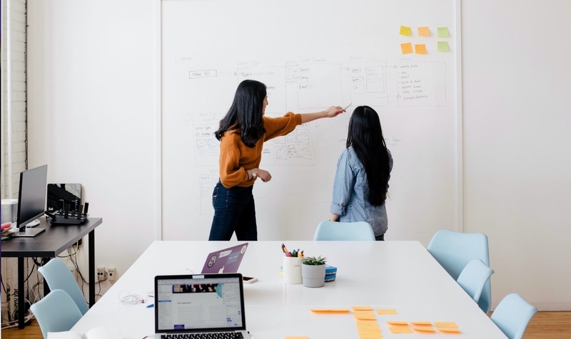 two girls pointing a whiteboard