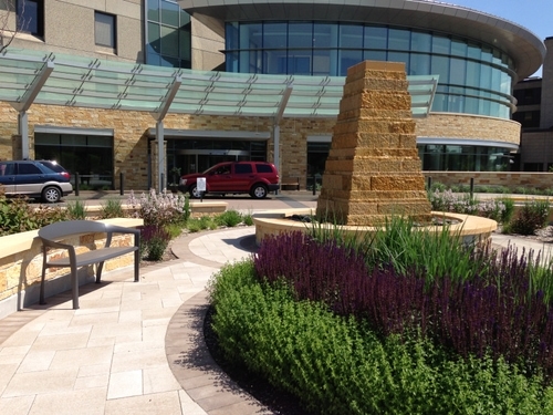 The tower-like water feature is a sentinel at the entry to the hospital and anchors a modest contemplative garden where lush plantings and low limestone seatwalls embrace users and buffer the energy of the parking lots, drive aisles and front door.