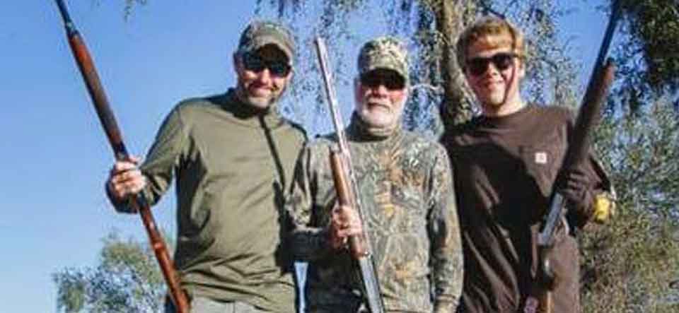 Guest hunters smiling in the field with their shotguns