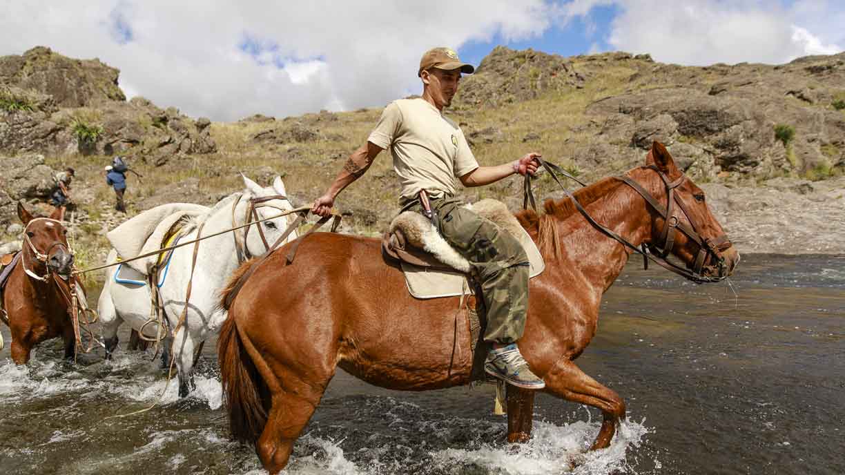 Riding across a mountain stream on a big game hunt