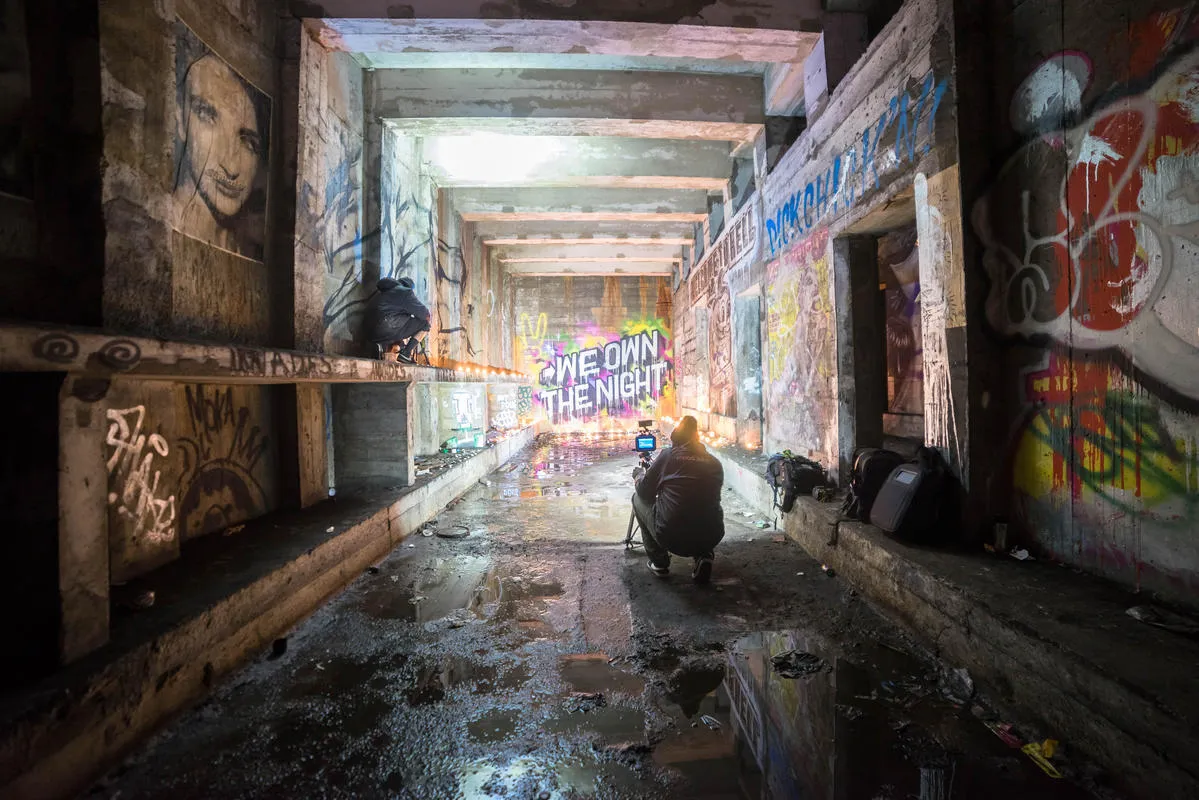 A photograph of a photographer kneeling and taking a picture on a camera at an abandoned subway station in NYC.