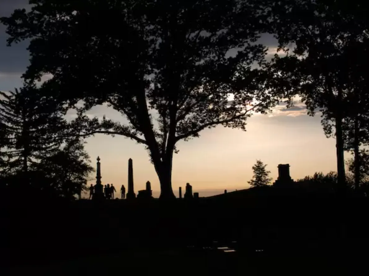 A dusk photo of headstones, trees, and the sky at Green-Wood Cemetery 