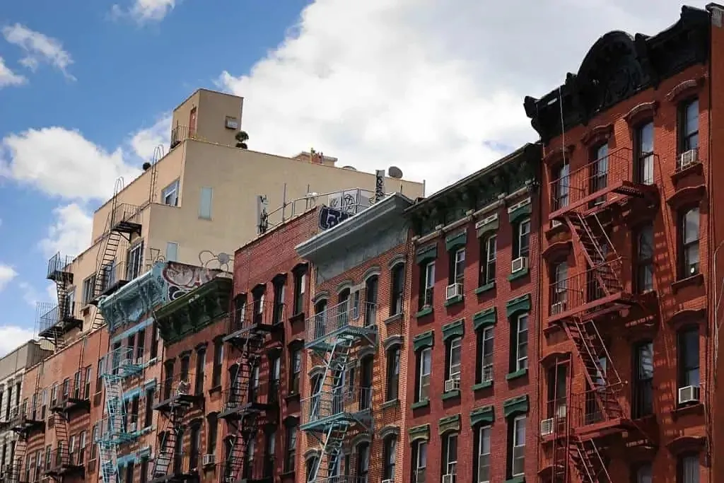 Photo of a block of brick buildings in the Lower East Side, set against a blue, partly-clouded sky.