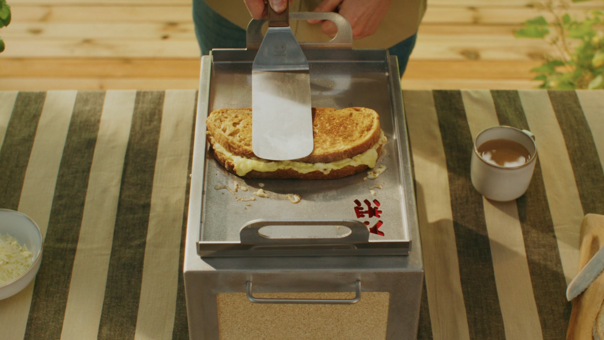 Two ribeye steaks on a Kasai Konro grill; a hand with red nails turns one with long stainless tongs.