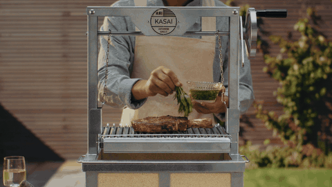 Marinated mushrooms flying mid-air out of a teal dish toward a Kasai grill; warm green bokeh behind.