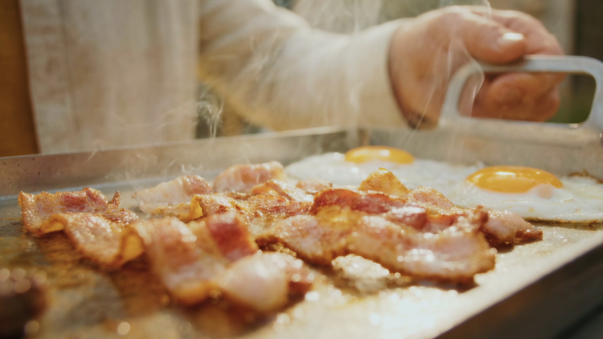 Three whole red romano peppers charring on a Kasai Konro grill; tongs lifting the front one.