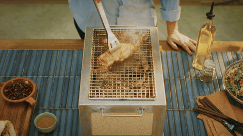 Overhead Kasai Konro grill with orange flames coming up through the grate, smoke rising, terracotta tiles below.