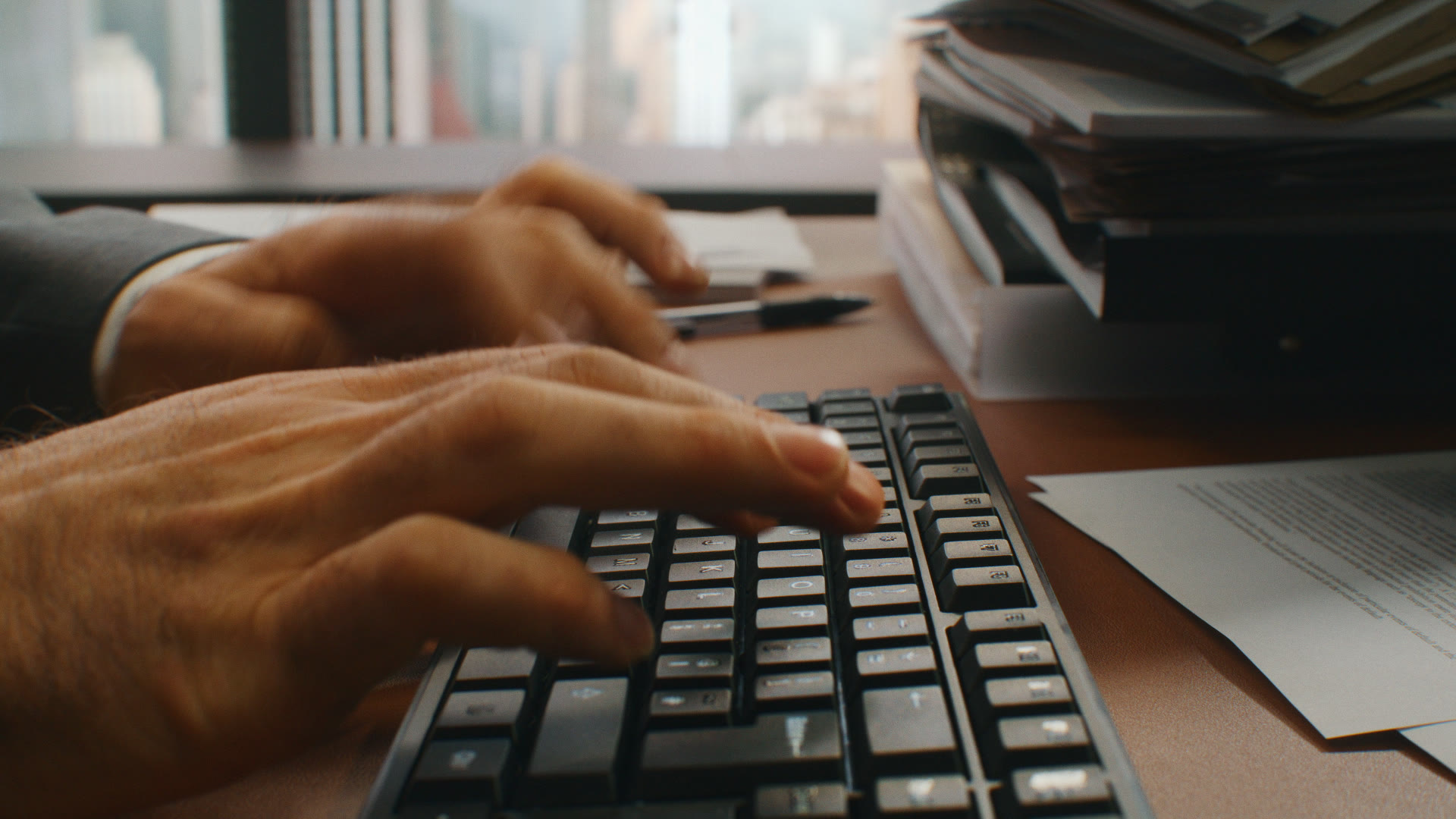 Side-on close-up of the lawyer's hands typing on the keyboard, NYC skyline out of focus behind.
